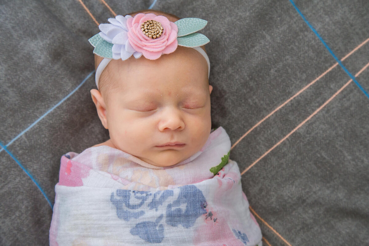 newborn baby girl, wrapped in flowered swaddle asleep on bed