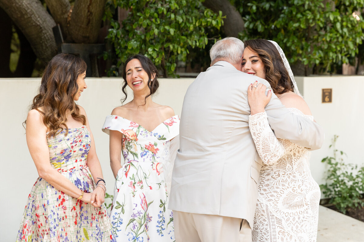 A bride hugging a man with bridesmaids standing behind them