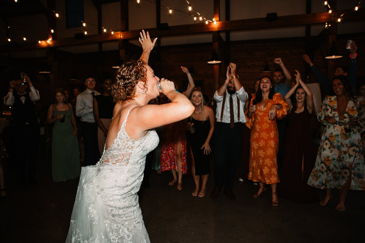 A bride raises a hand while taking a shot on the dance floor to applause