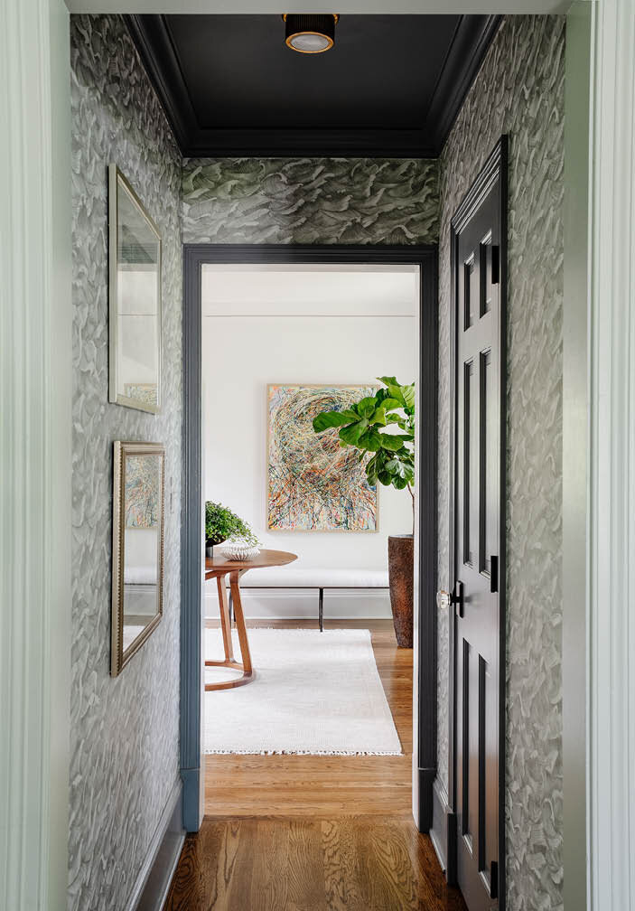 See the small corridor next to the powder room in this Hingham home, featuring grey wave wallpaper by Cole & Son, perfectly complementing the coastal location and leading to the foyer.