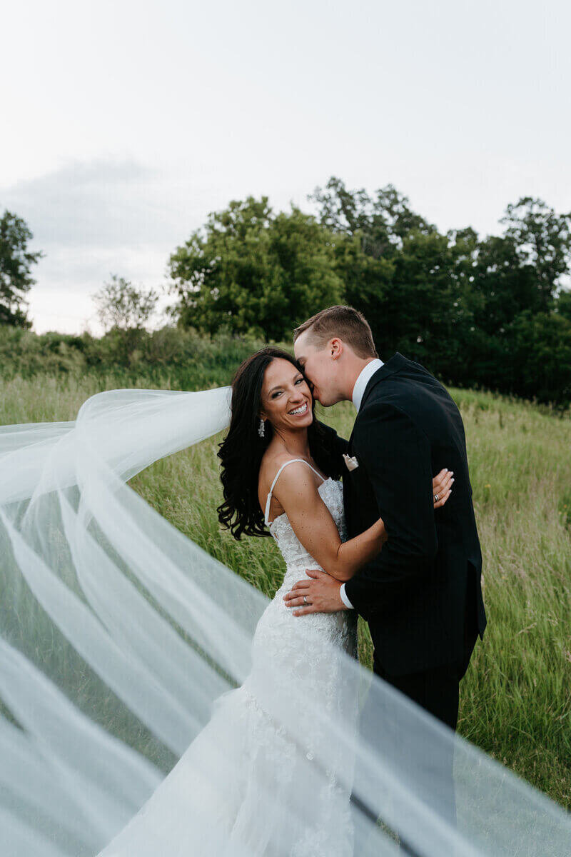 Groom kissing bride with veil flying in the wind planned by luxury wedding planner chicago