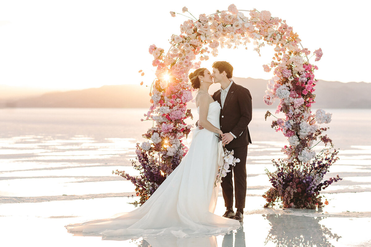 Utah Wedding Photographers capture bride and groom standing at floral arch during wedding at the Salt Flats