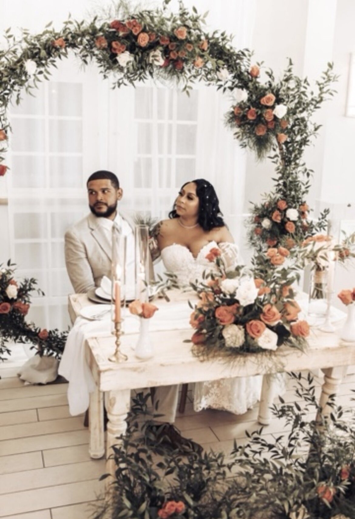 bride and groom sitting at a table surrounded by orange and white roses