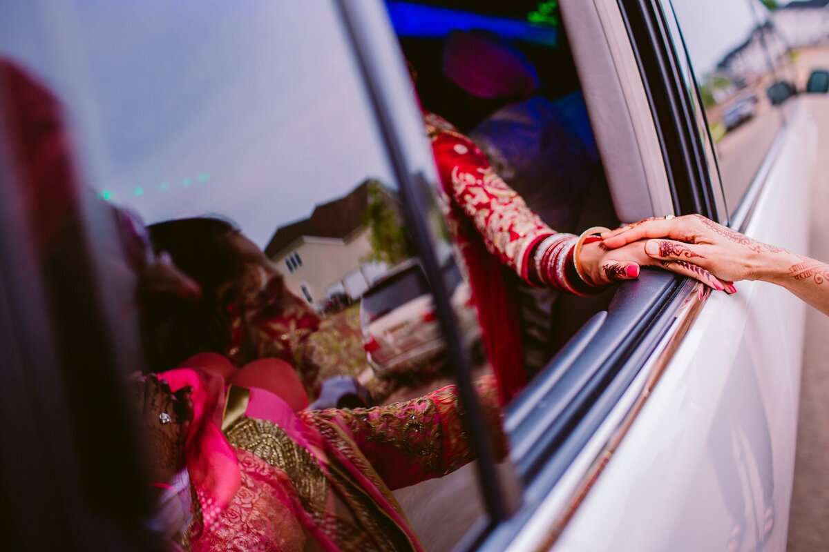 A sikh bride and her mother hold hands on the car window as she exits from the wedding ceremony during the doli vidai