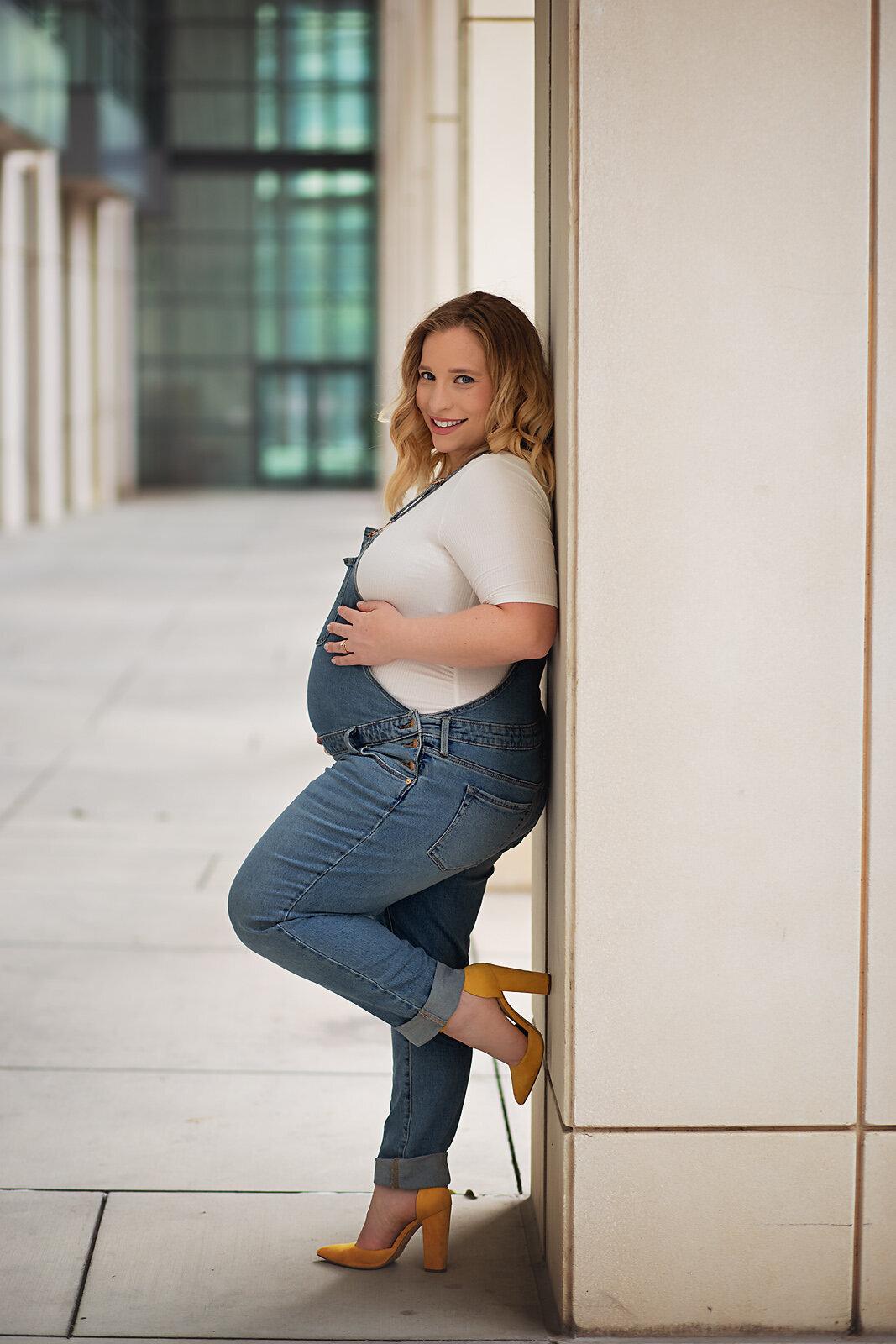casual maternity session overalls mom leaning on pillar charlotte convention center