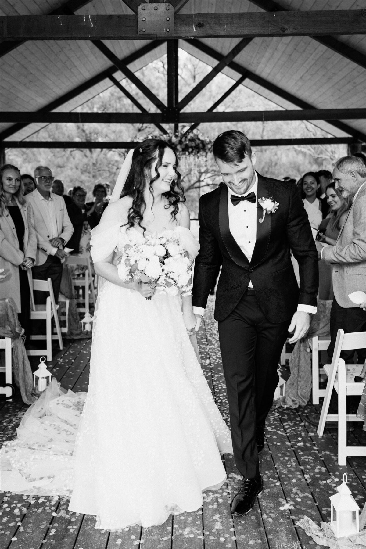 The newlyweds share a tender kiss as they exit the ceremony, radiating love and joy in their post-nuptial bliss.