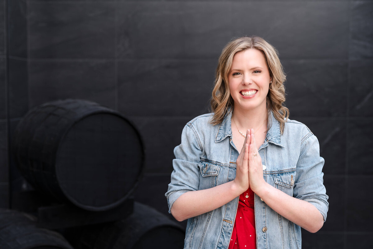 Female entrepreneur with hands together in gratitude in denim jacket and red dress downtown Kelowna.