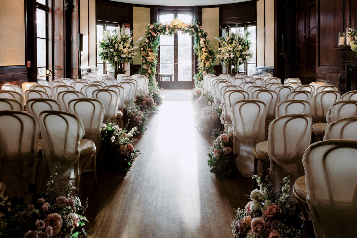 Row of seats with and aisle in the middle and a flowered arch in front.