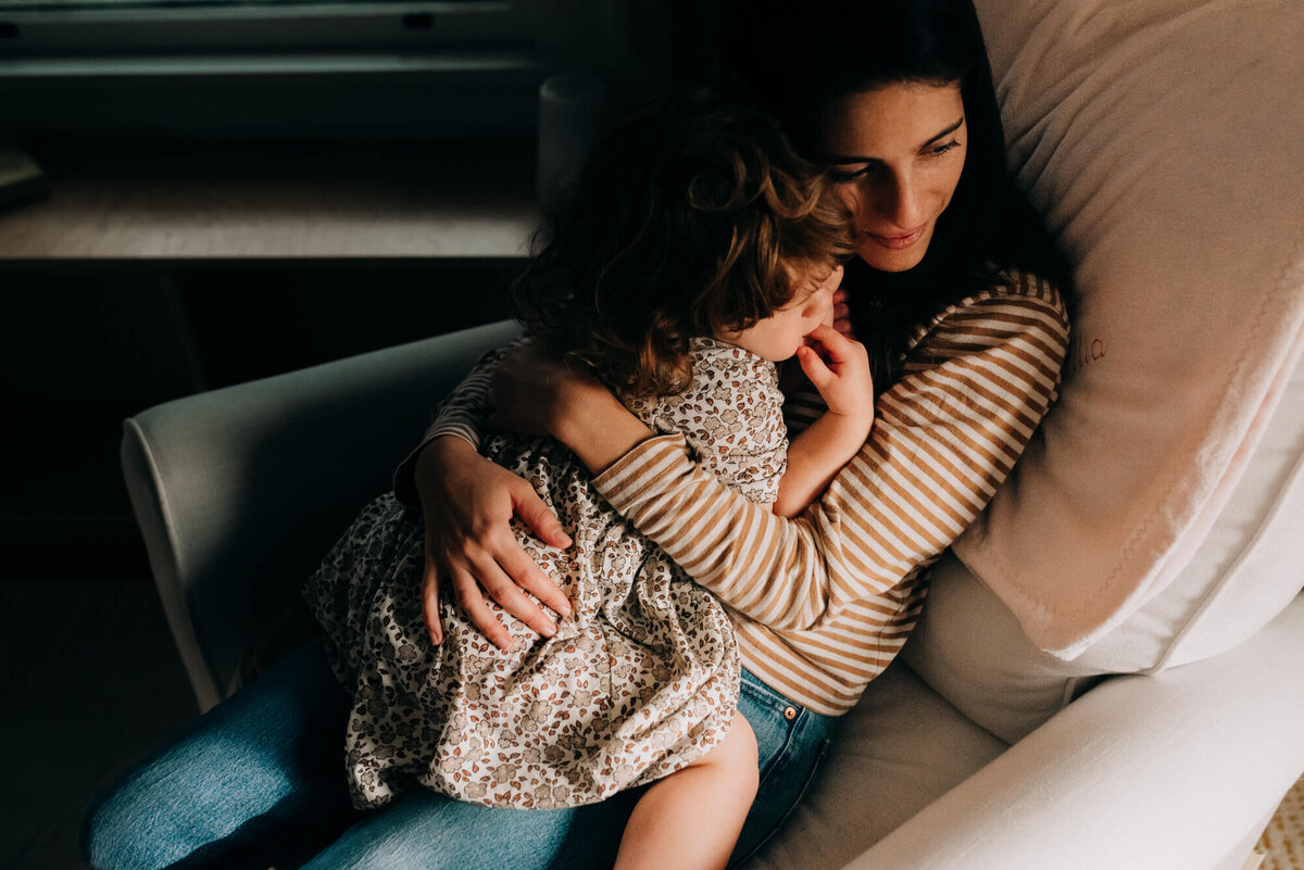 A mother snuggles her red haired toddler in a cream colored rocker during their photoshoot with Allison Wolf, Boston Family Photographer
