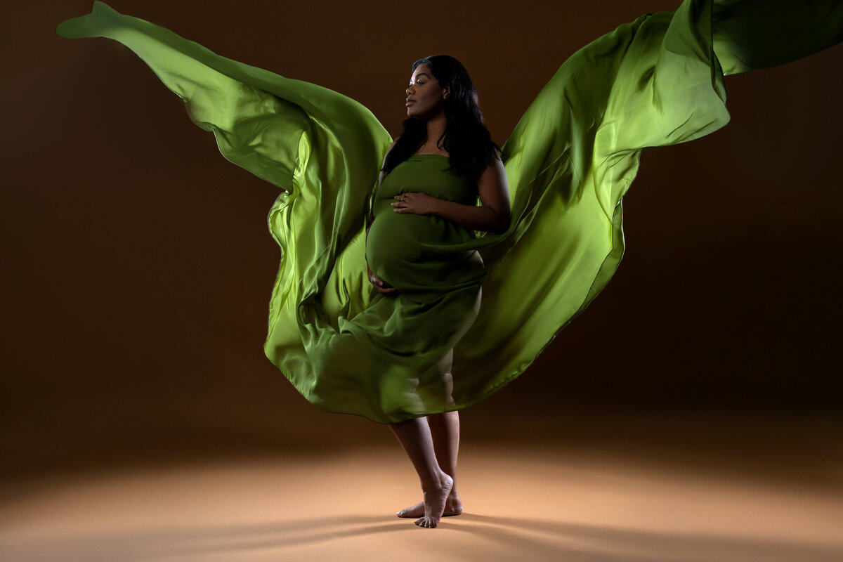 Mom to be posing for maternity session with green maternity floating in air