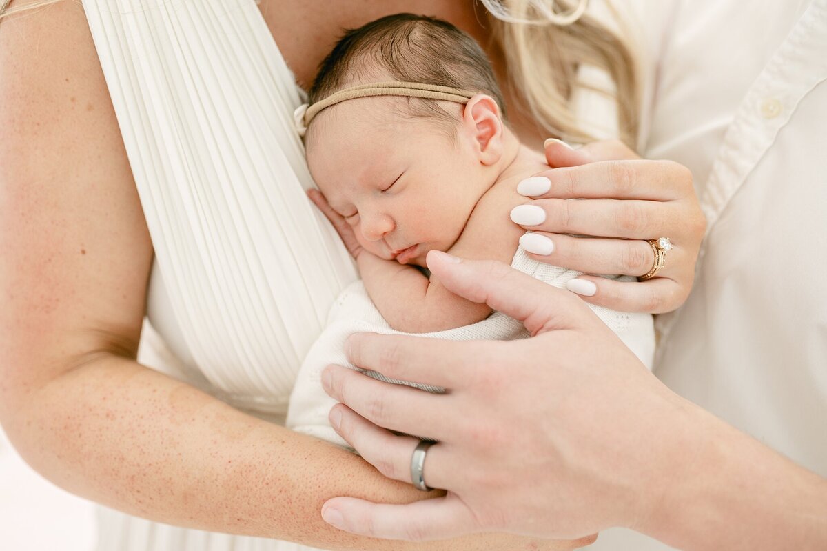 Close up photograph of baby on mom's chest with dad's hands on baby's back