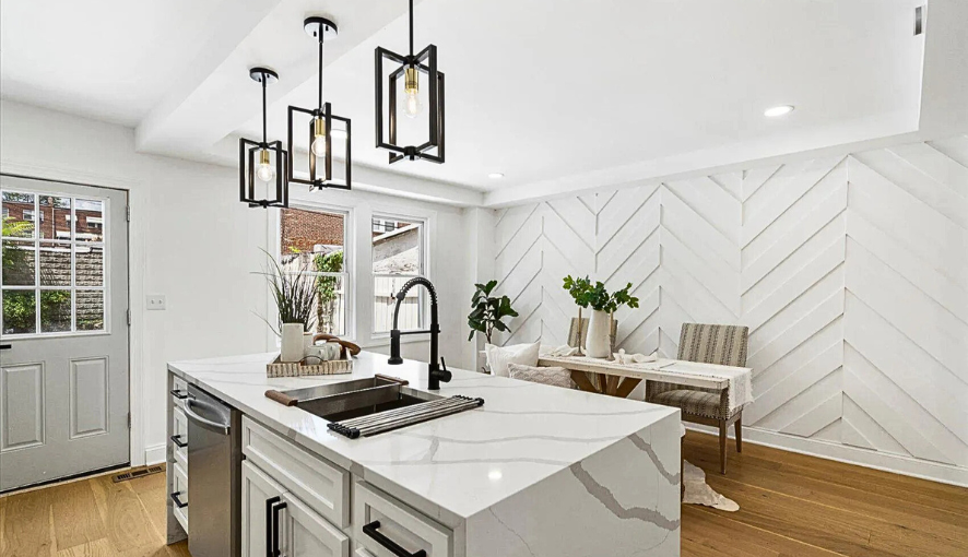 Contemporary kitchen and dining remodel featuring a quartz waterfall island, bold pendant lighting, and a custom chevron accent wall—designed to elevate style and maximize functionality.