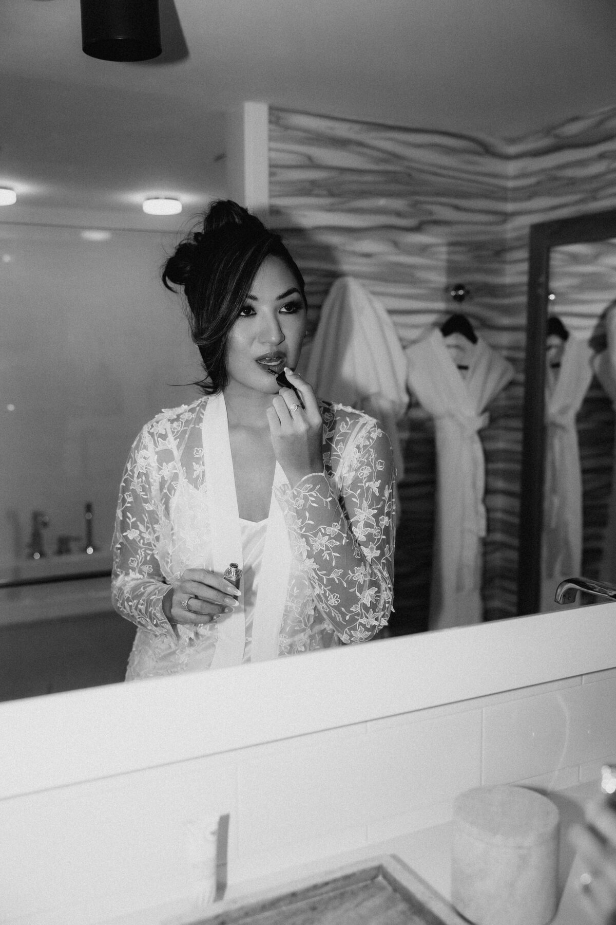 Bride fixing lipstick in the hotel bathroom mirror wearing lace robe