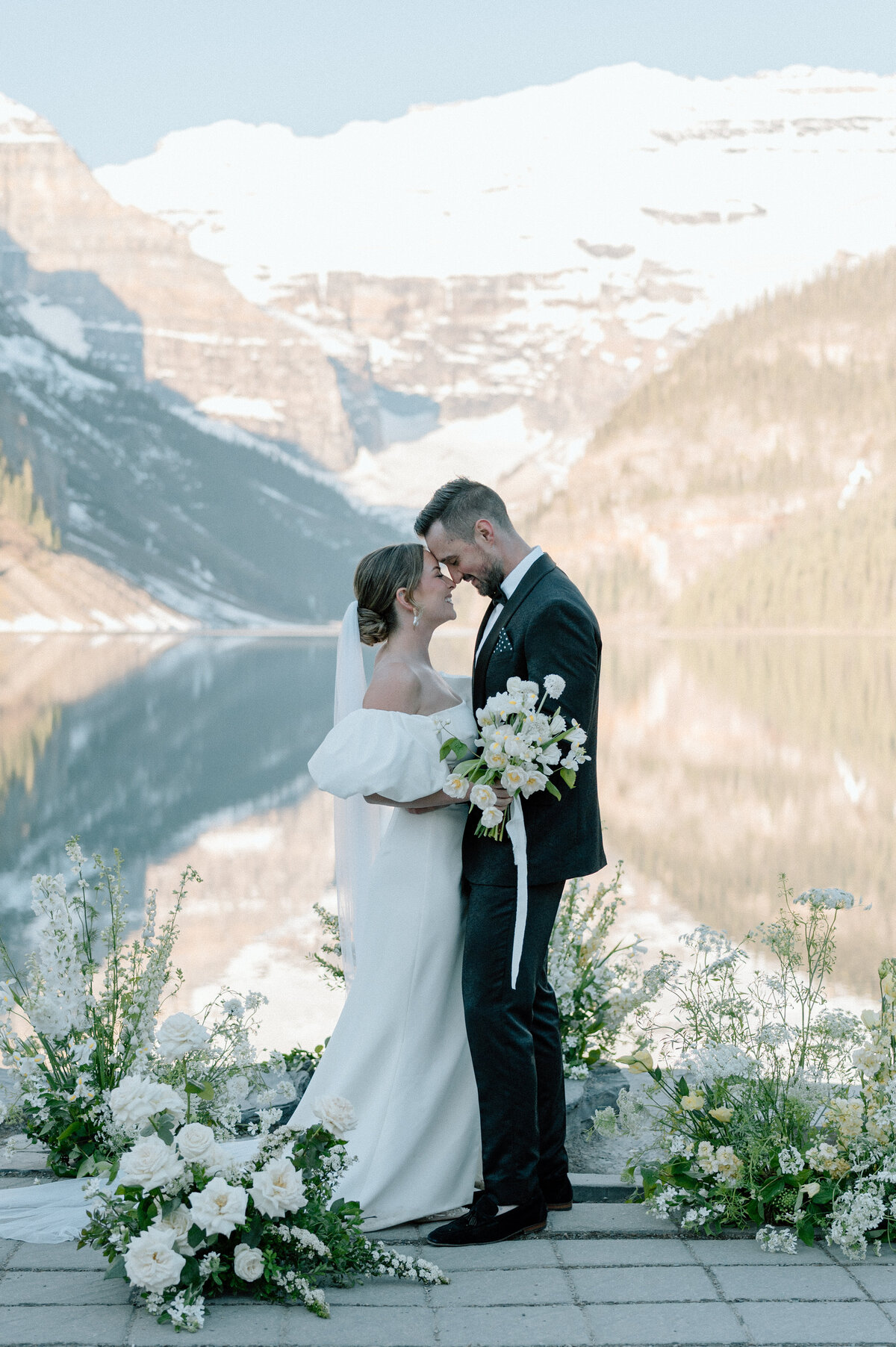 Elegant wedding portrait with bride and groom holding white bouquet at Lake Louise