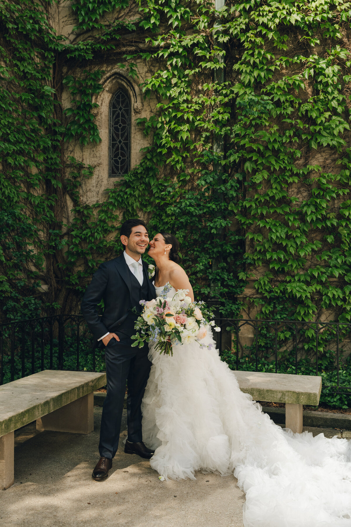 A bride and groom looking at each other smiling with green ivy in the background. 