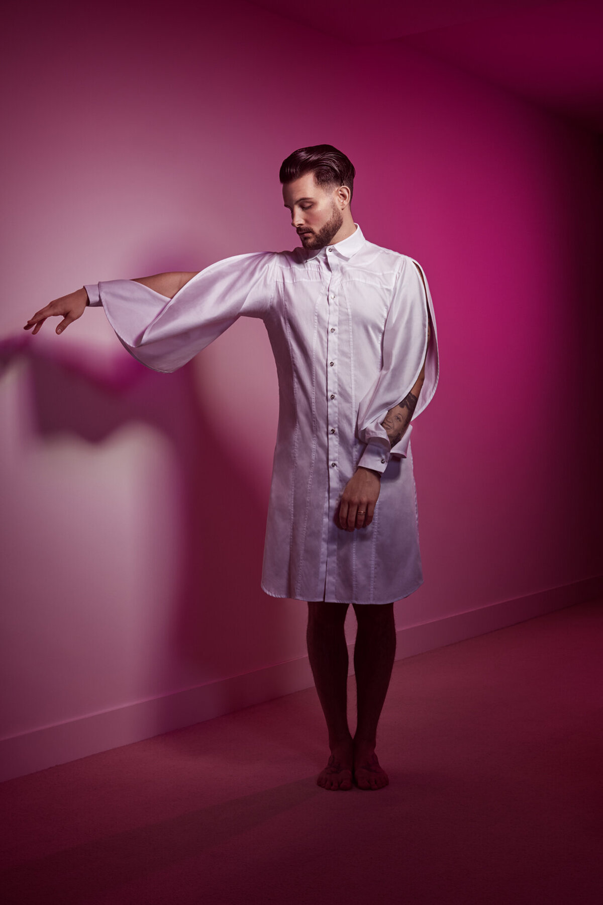 High-fashion portrait of Nico Tortorella in a dramatic pose, set against a pink background, shot by Ylva Erevall.