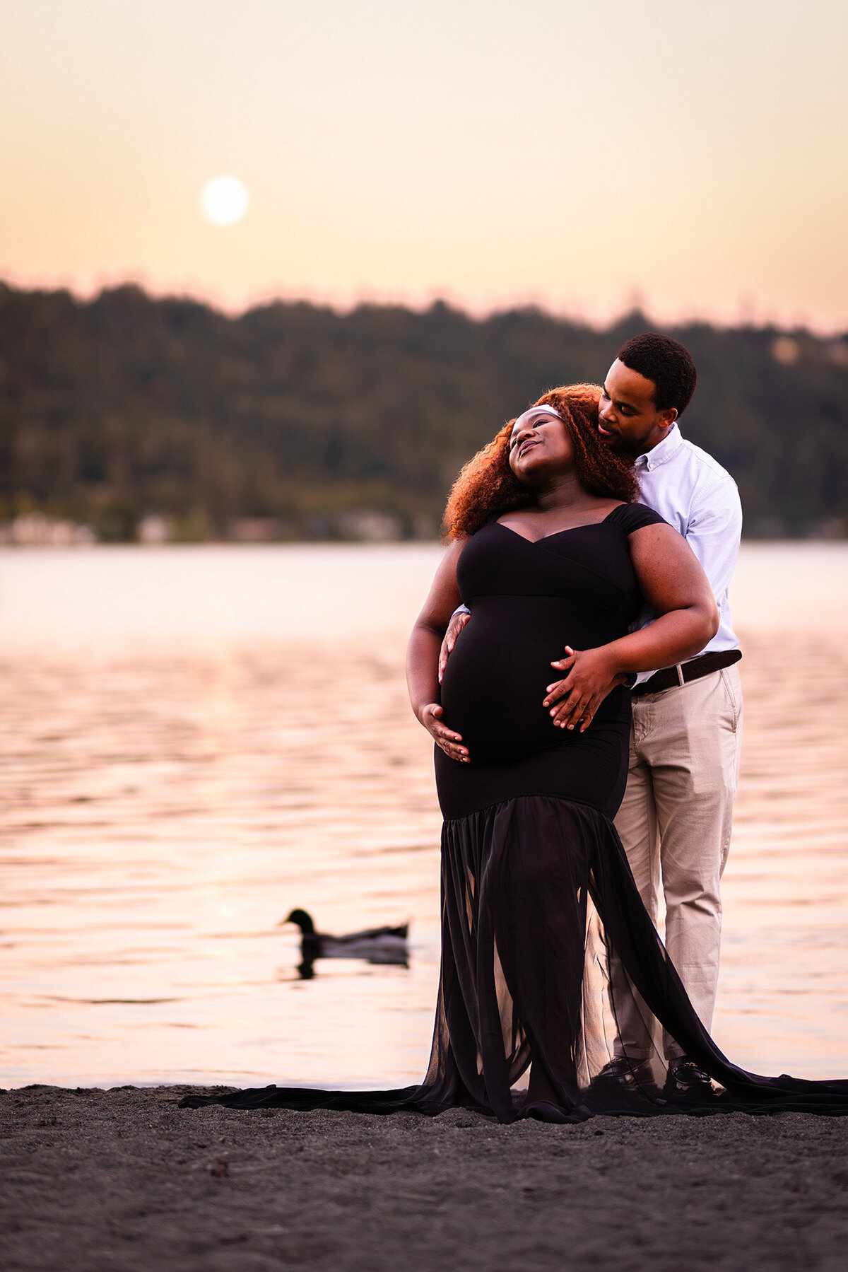 An expectant couple embracing in front of Lake Sammamish, against a moonlit sky.