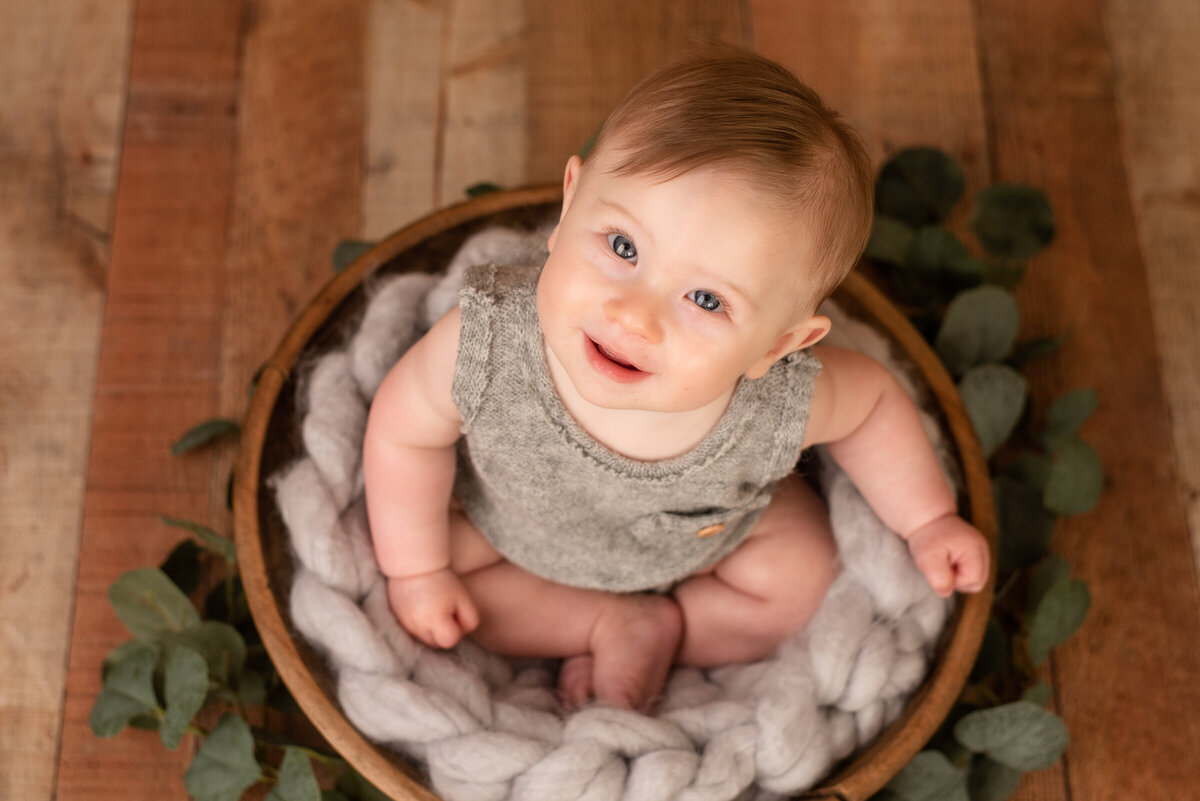 Little boy smiles up at the camera, sitting in wooden bowl