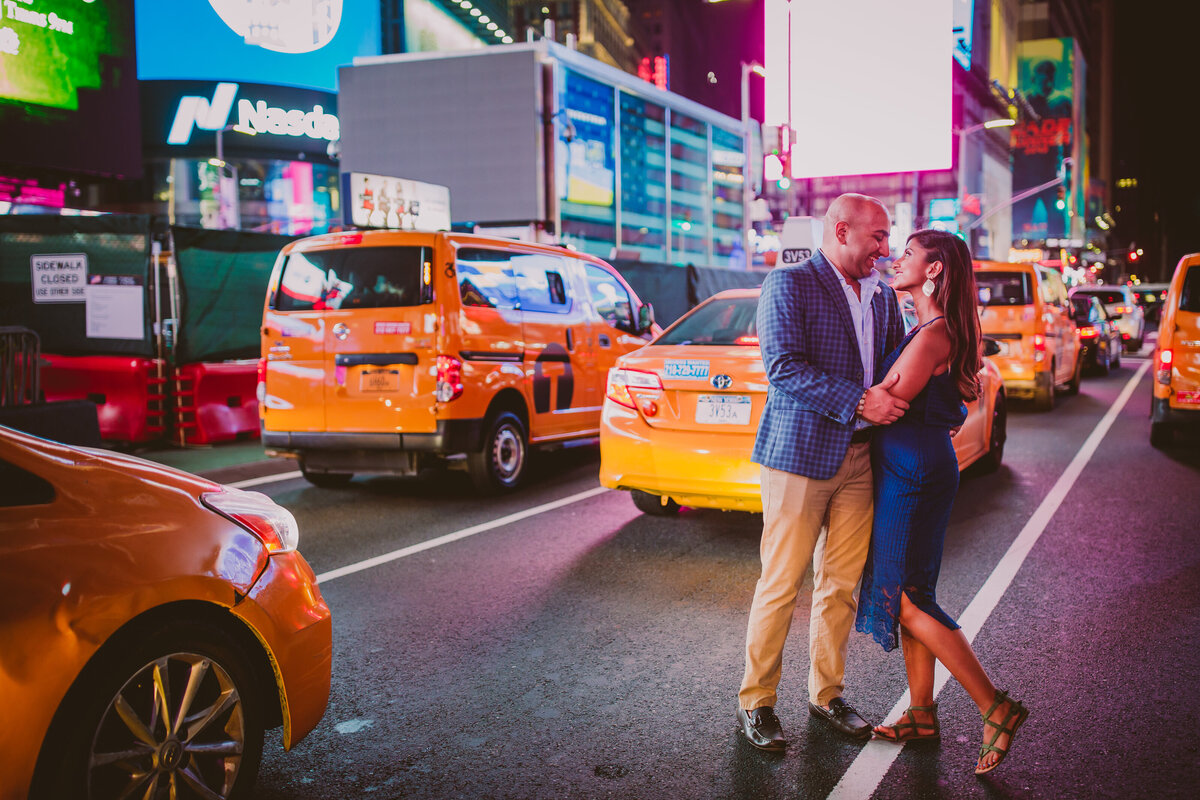 A couple standing in the middle of the street in times square in front of taxis