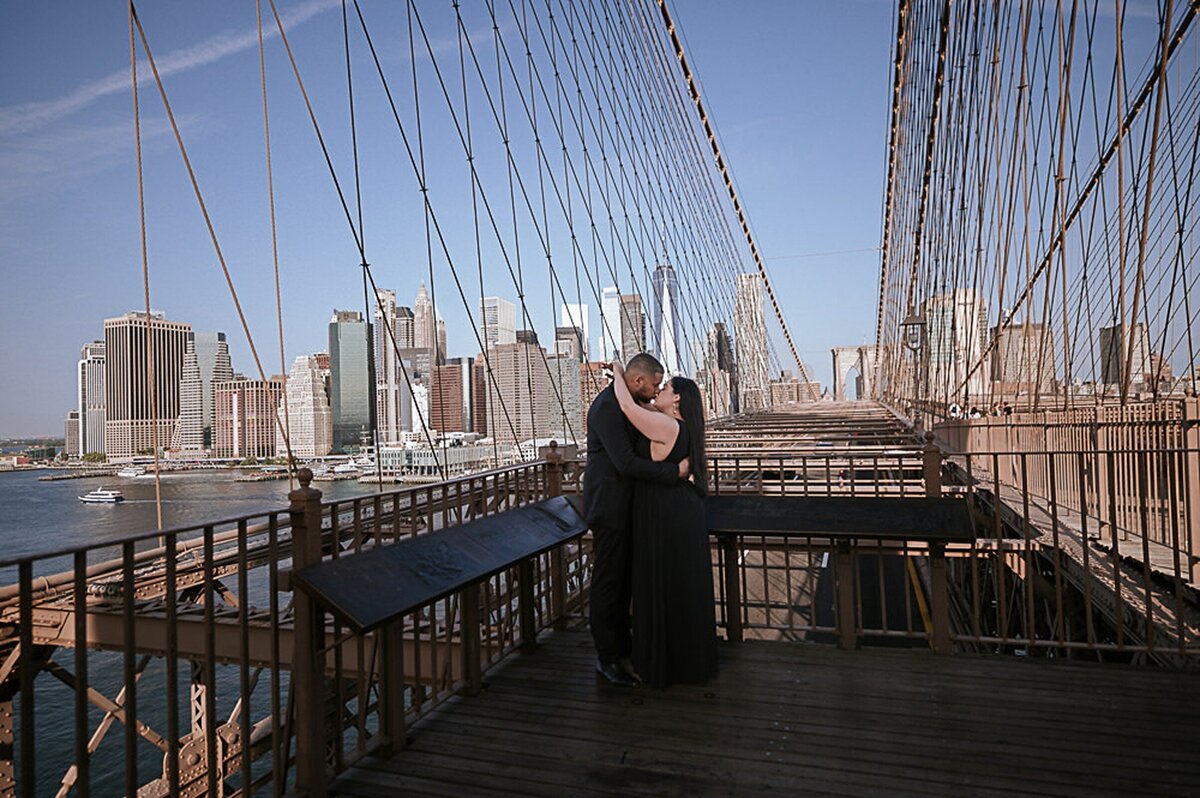 Elegant latino couple dressed in black tie hugging on the Brooklyn Bridge.