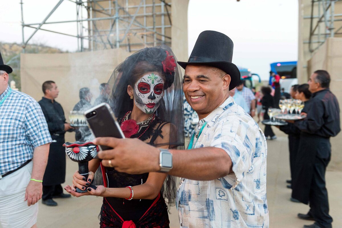 Man at large celebration poses with day of the dead talent for a selfie.