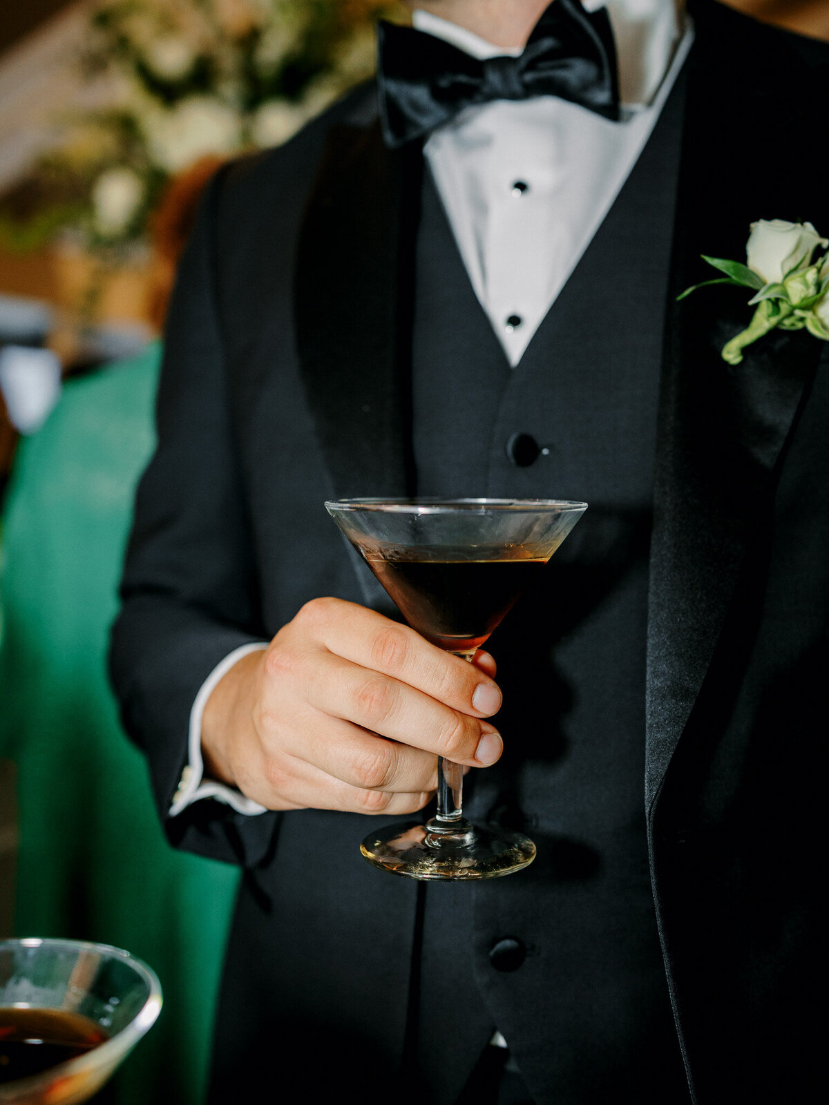 Wedding guest in black tux and bow tie holding an espresso martini during a destination wedding in New England