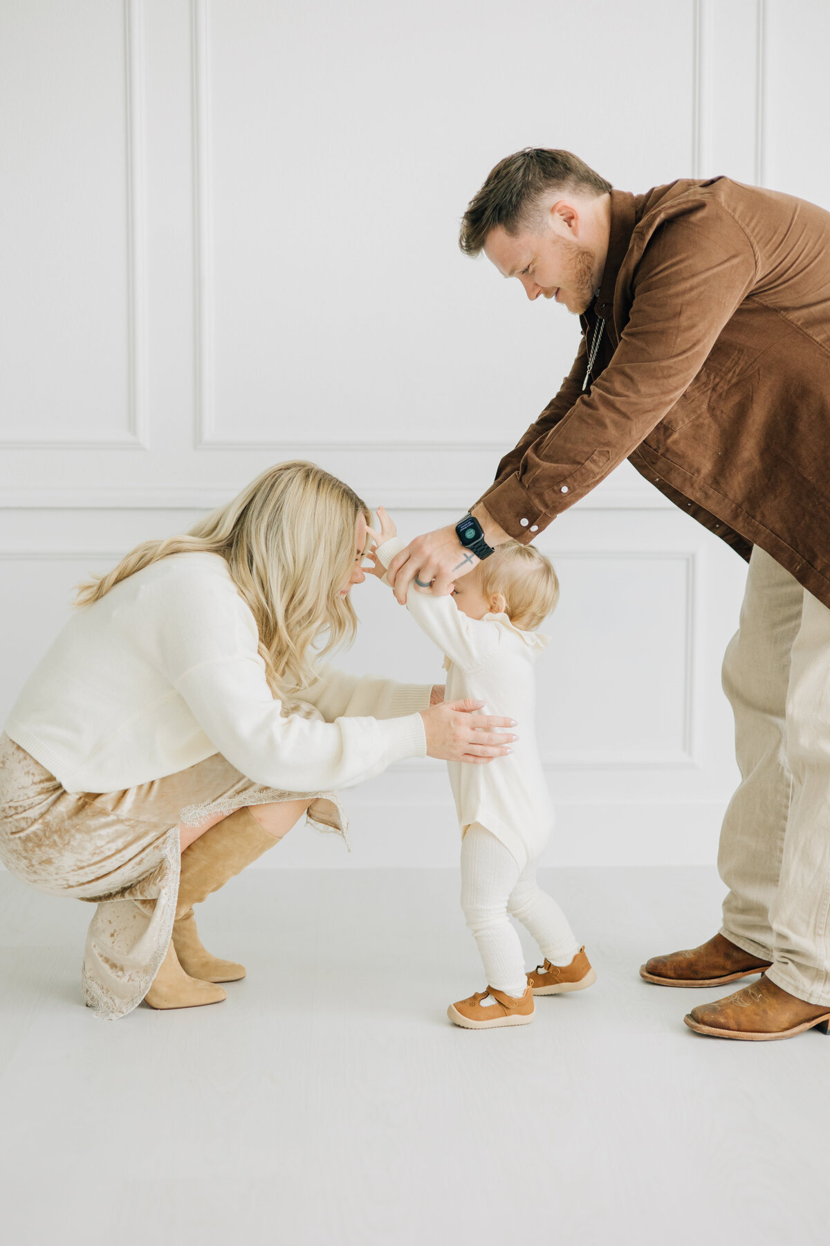 Studio one-year old girl session with family. An image showcasing a father helping his little girl to walk. Studio located in Lewisville, TX,