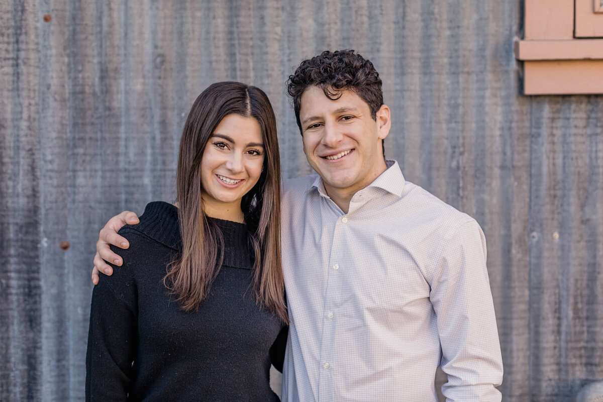 A brother and sister hugging and smiling at the camera against a metal wall at Irvine Ranch Park.