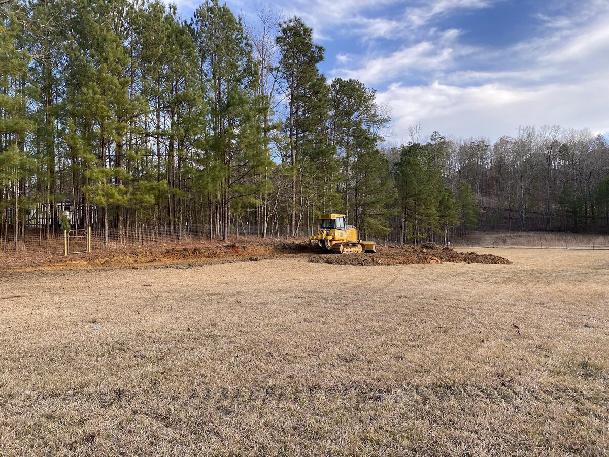 heavy-machinery-moving-dirt-in-large-filed-next-to-treeline