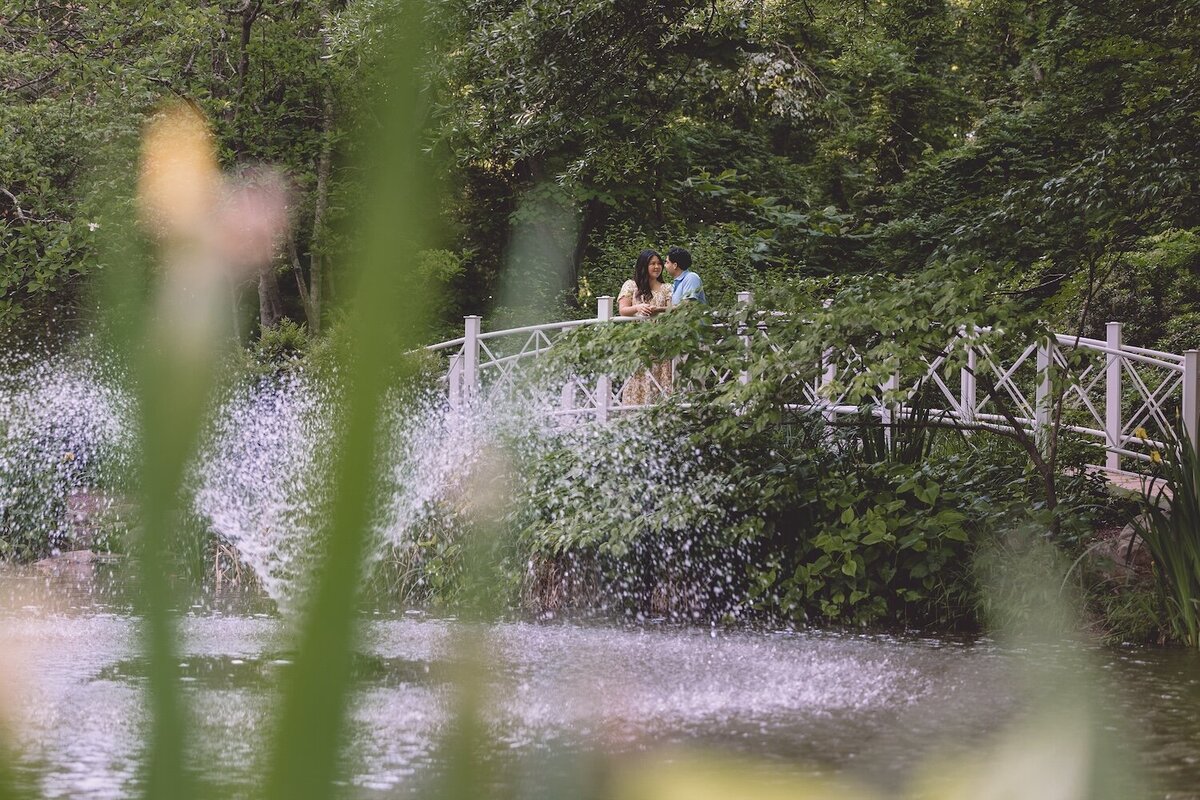 Dreamy photo of couple standing by a bridge through wildflowers.