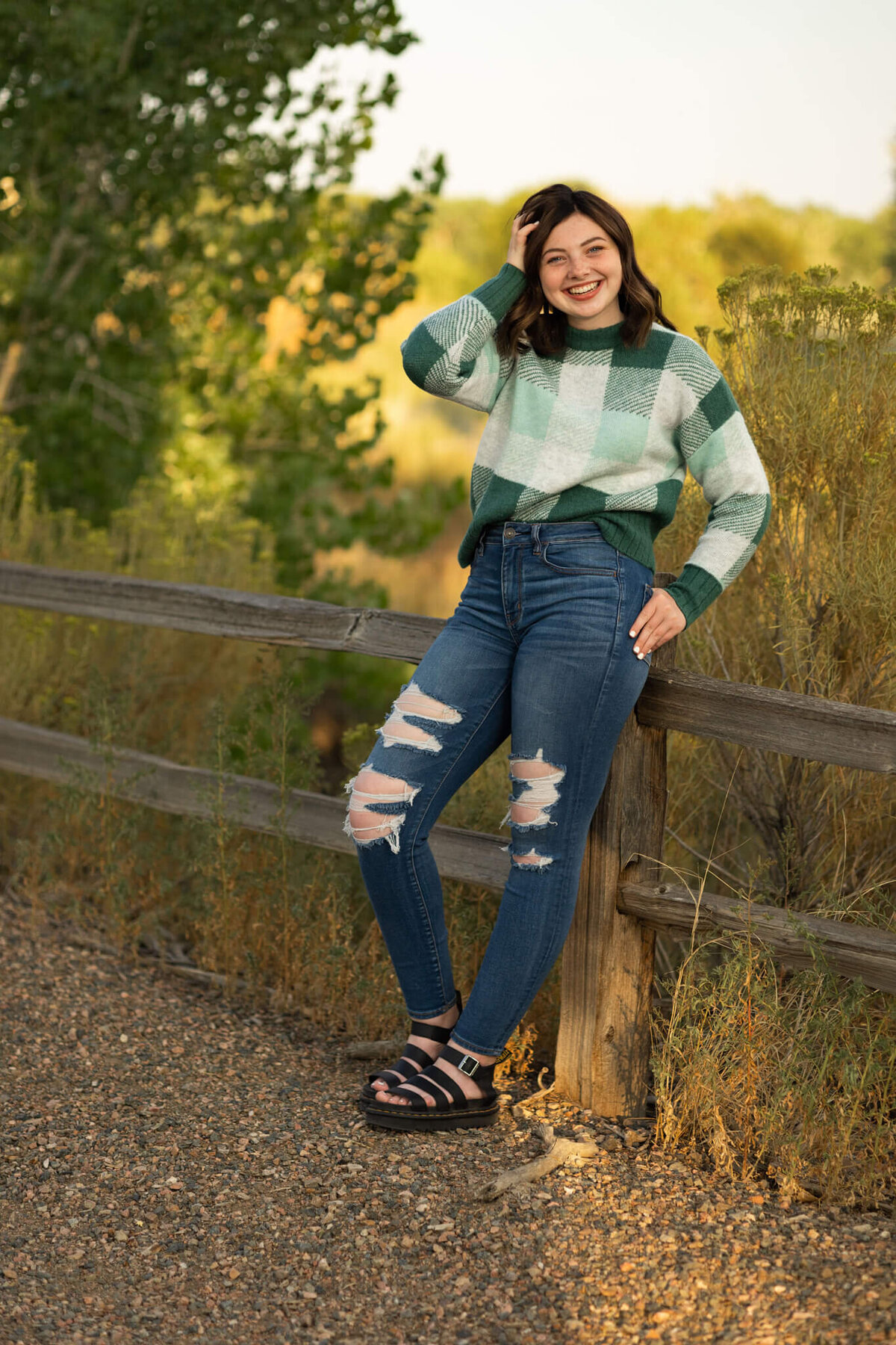 teenage girl in green sweater and jeans leaning against a fence on a trail