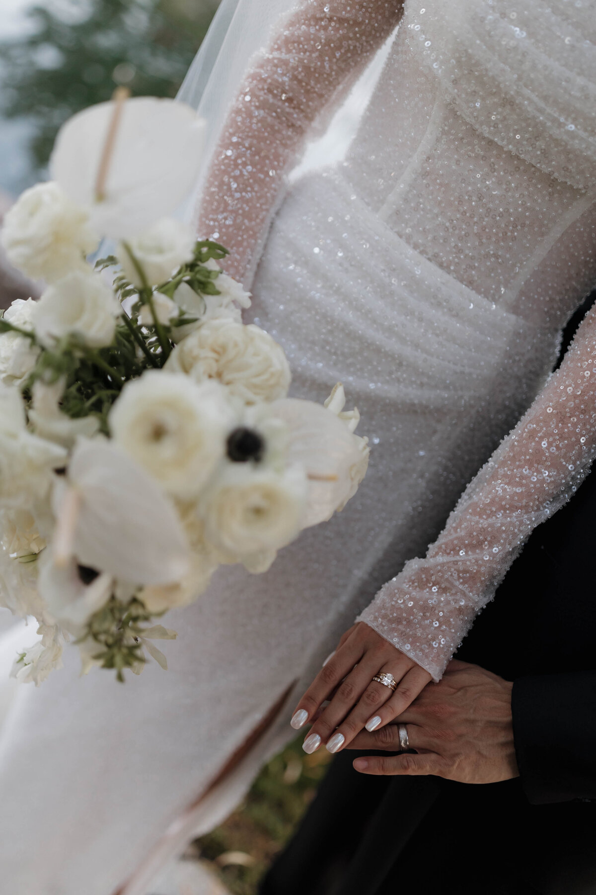 A close-up of the couple’s hands showing their wedding rings, with a beautiful bouquet in the background.