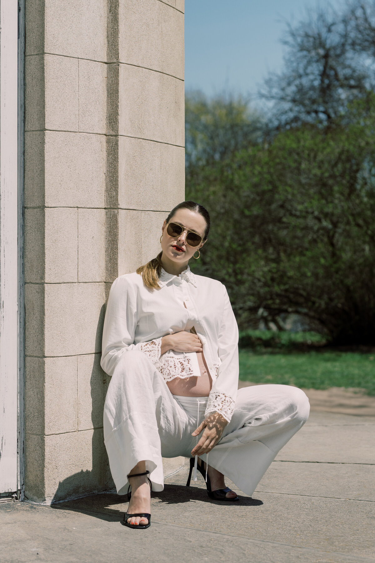 Candid black-and-white fashion-inspired maternity shot with the subject leaning against a sunlit exterior wall
