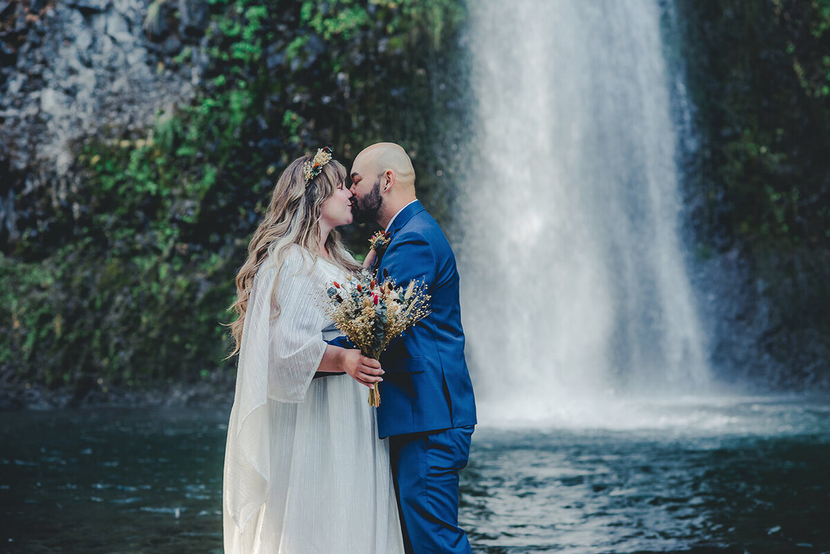 bride and groom kissing by waterfall