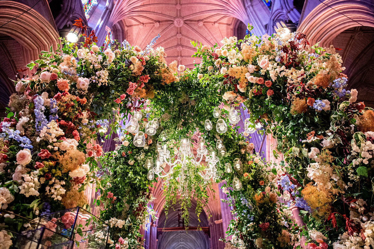 A grand stone staircase leading up to an ornate building entrance decorated with a floral arrangement of white flowers and candles. The entrance features large columns, an arch with intricate metalwork, and a large hanging lantern.