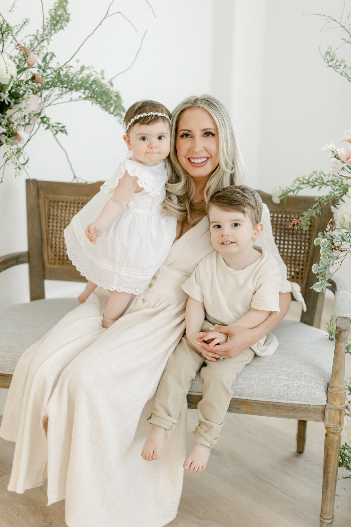 Mom holding her two children on a beautiful bench surrounded by flowers in Family Photographer South Jersey Tara Federico's Haddonfield NJ Studio