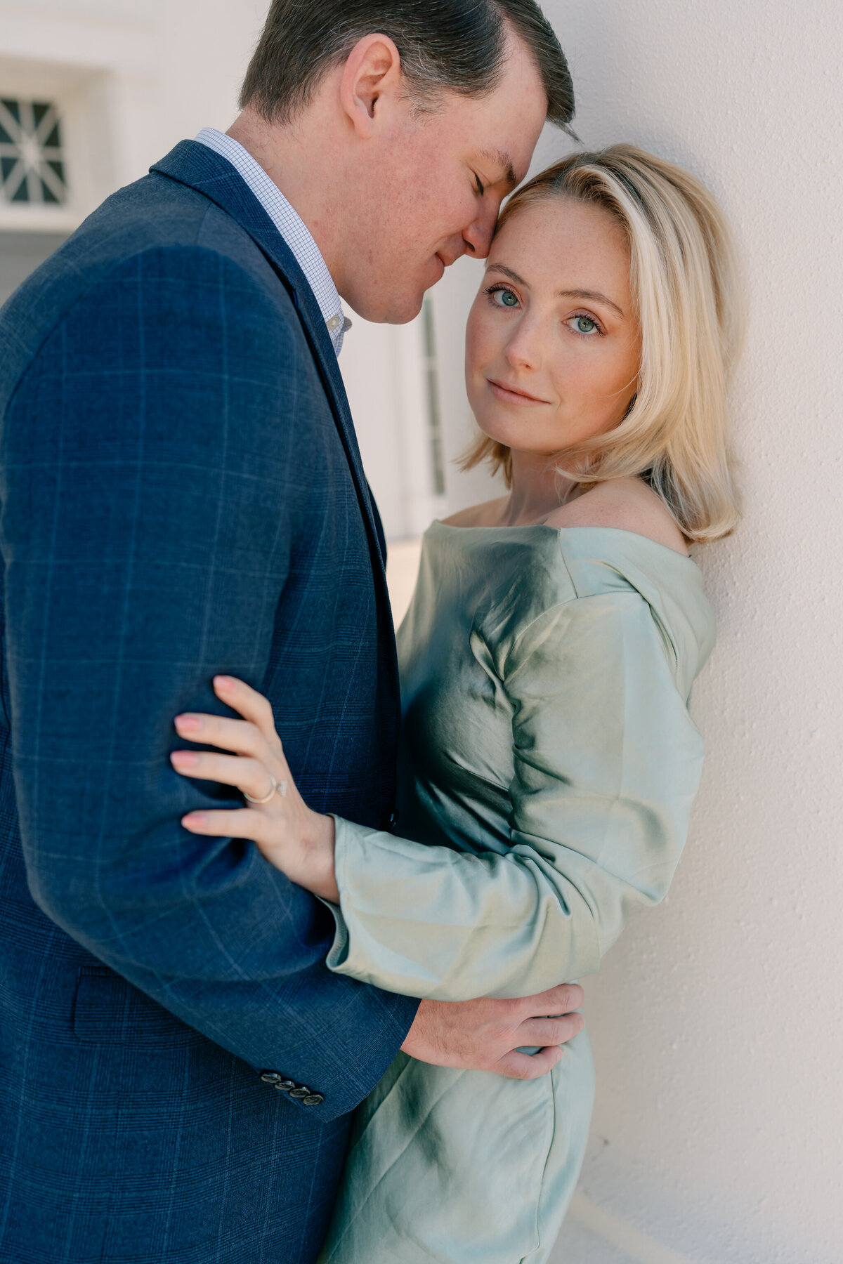 Virginia State Capitol Building Engagement Photos Richmond VA | newly engaged couple in green dress and blue suit lean against white column as the groom-to-be nuzzles into his future wife