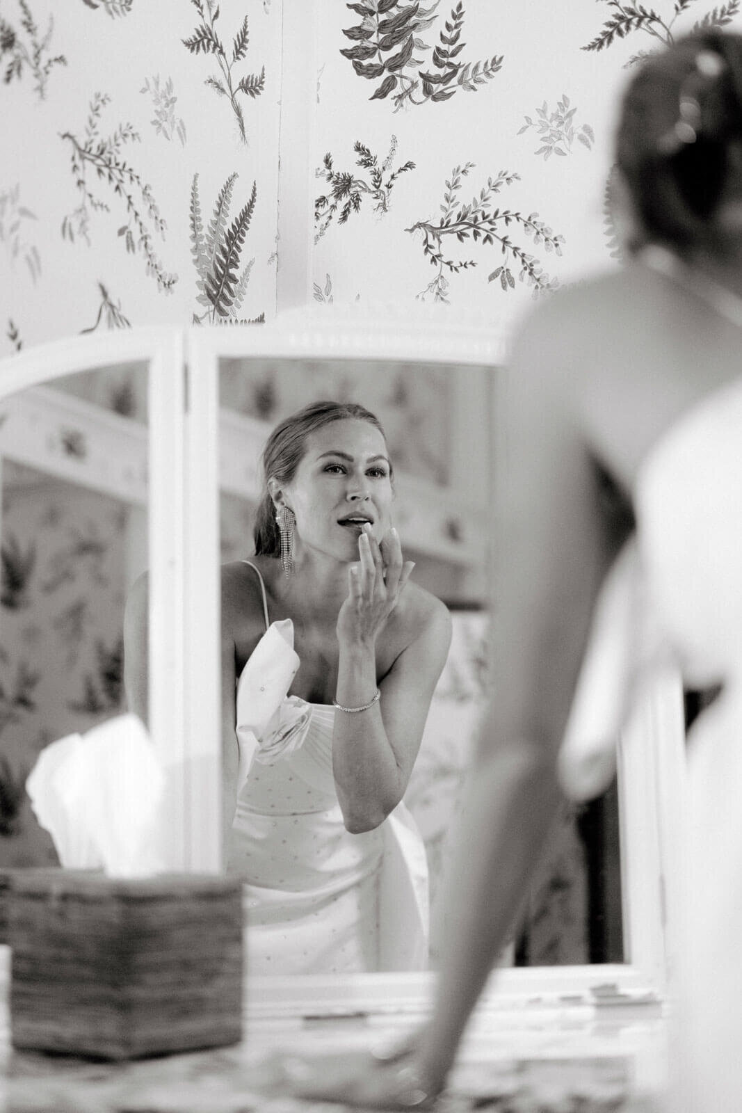 The pretty bride is re-touching her make-up in front of the mirror at The Ausable Club, NY. Image by Jenny Fu Studio