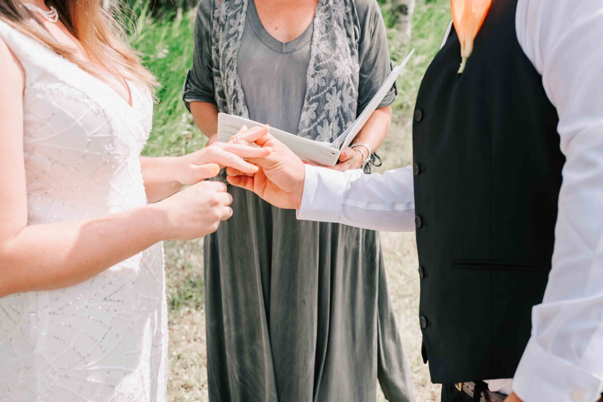 Groom placing ring on bride's finger.