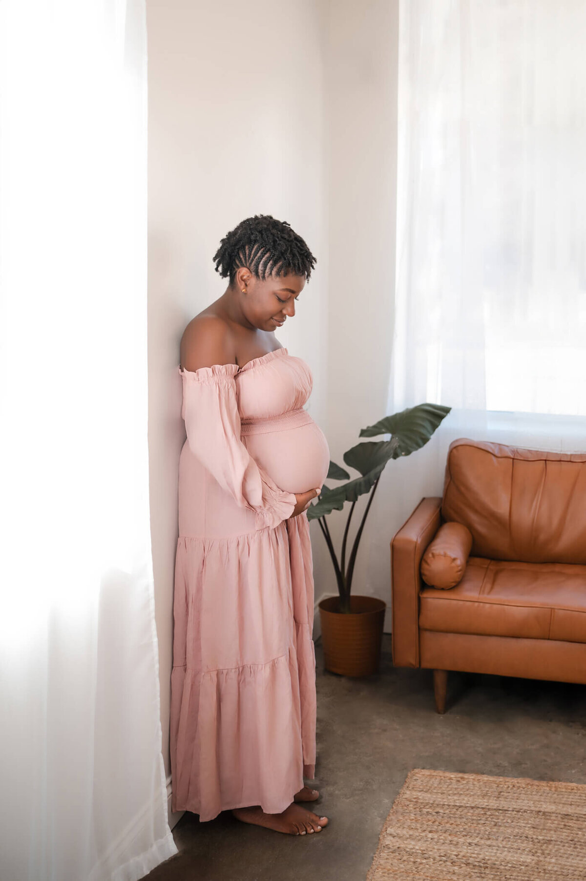 side view of woman holding her baby bump next to a window while posing for professional maternity photos with Kim Pickett