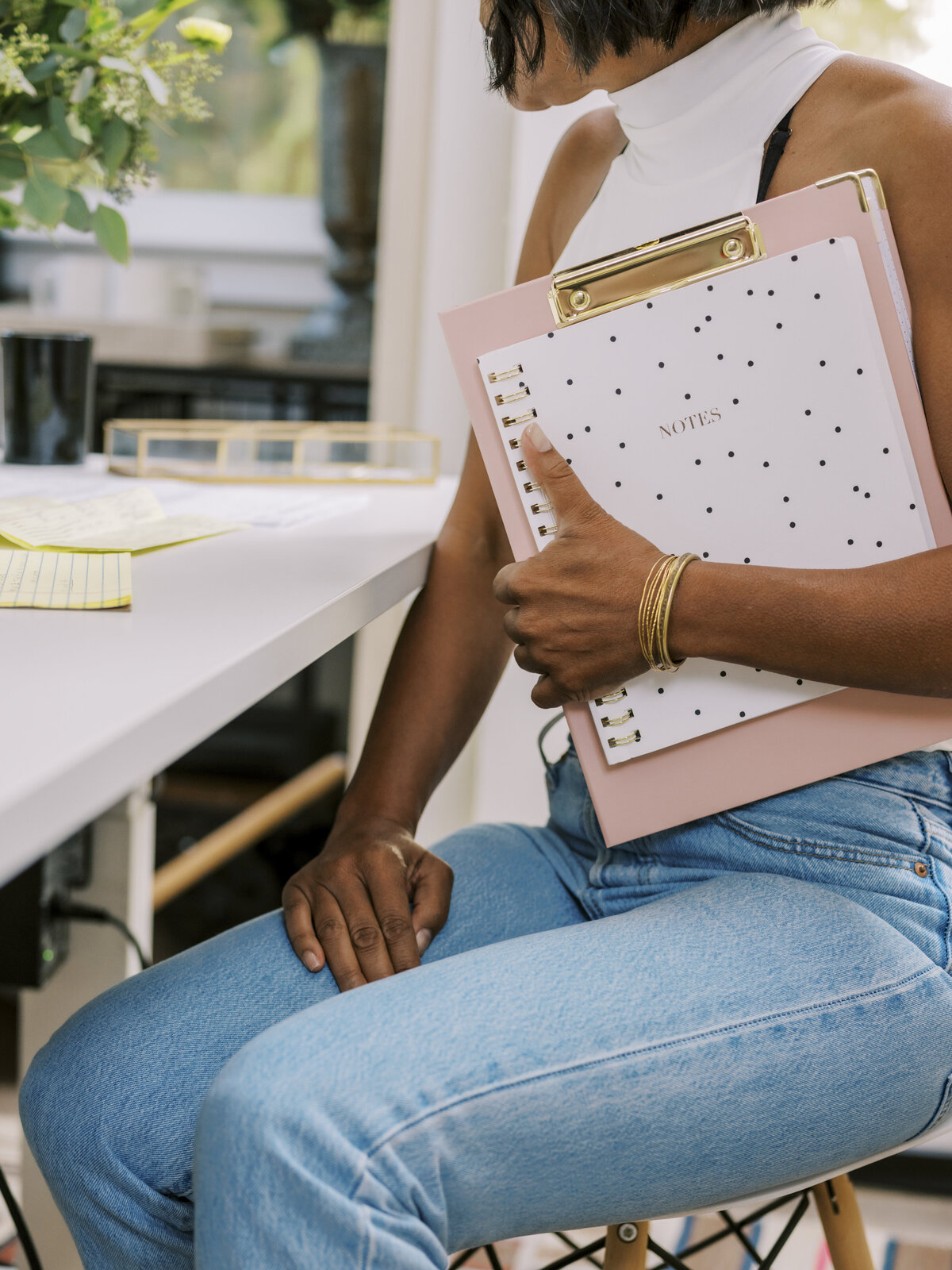 Close-up of Black woman in white top holding a pink clipboard while seated at desk in NYC brand shoot.