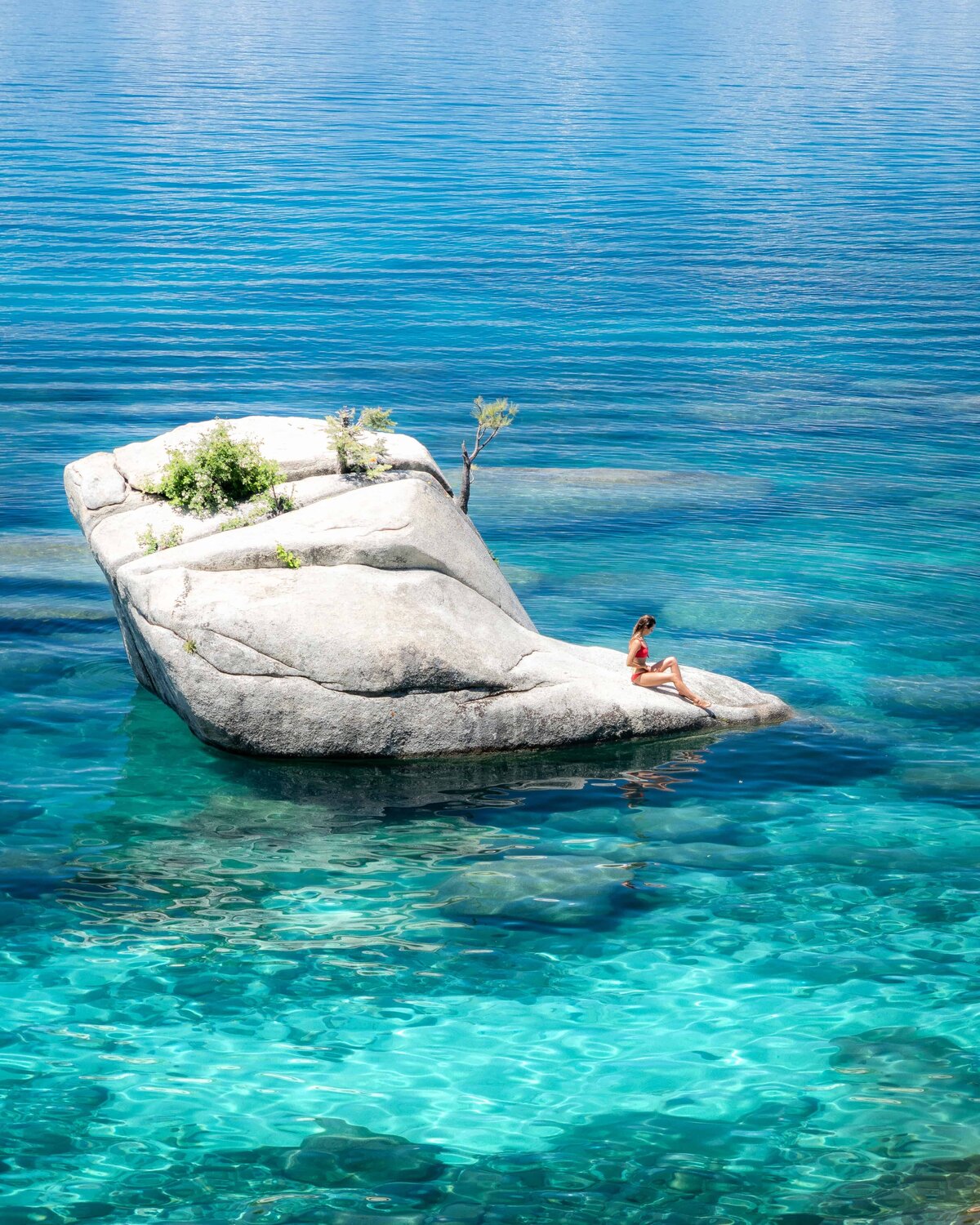 Woman in a red swimsuit sitting on a rock in the middle of Lake Tahoe