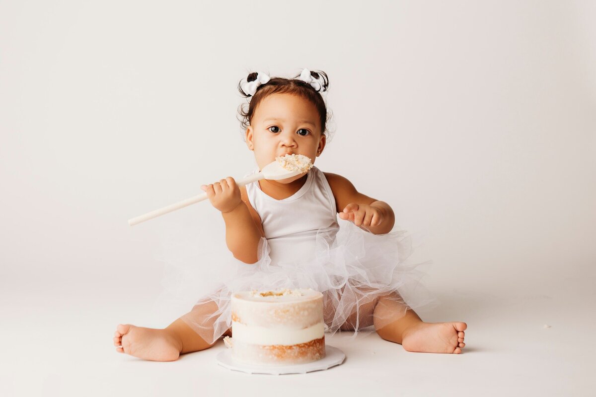 infant eating cake on white backdrop