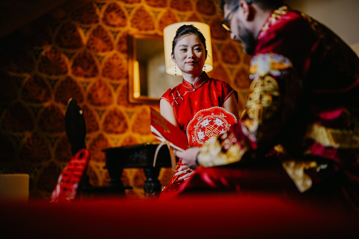 Bride in red dress and groom in Chinese outfit during ceremony, wedding photographer Tuscany.