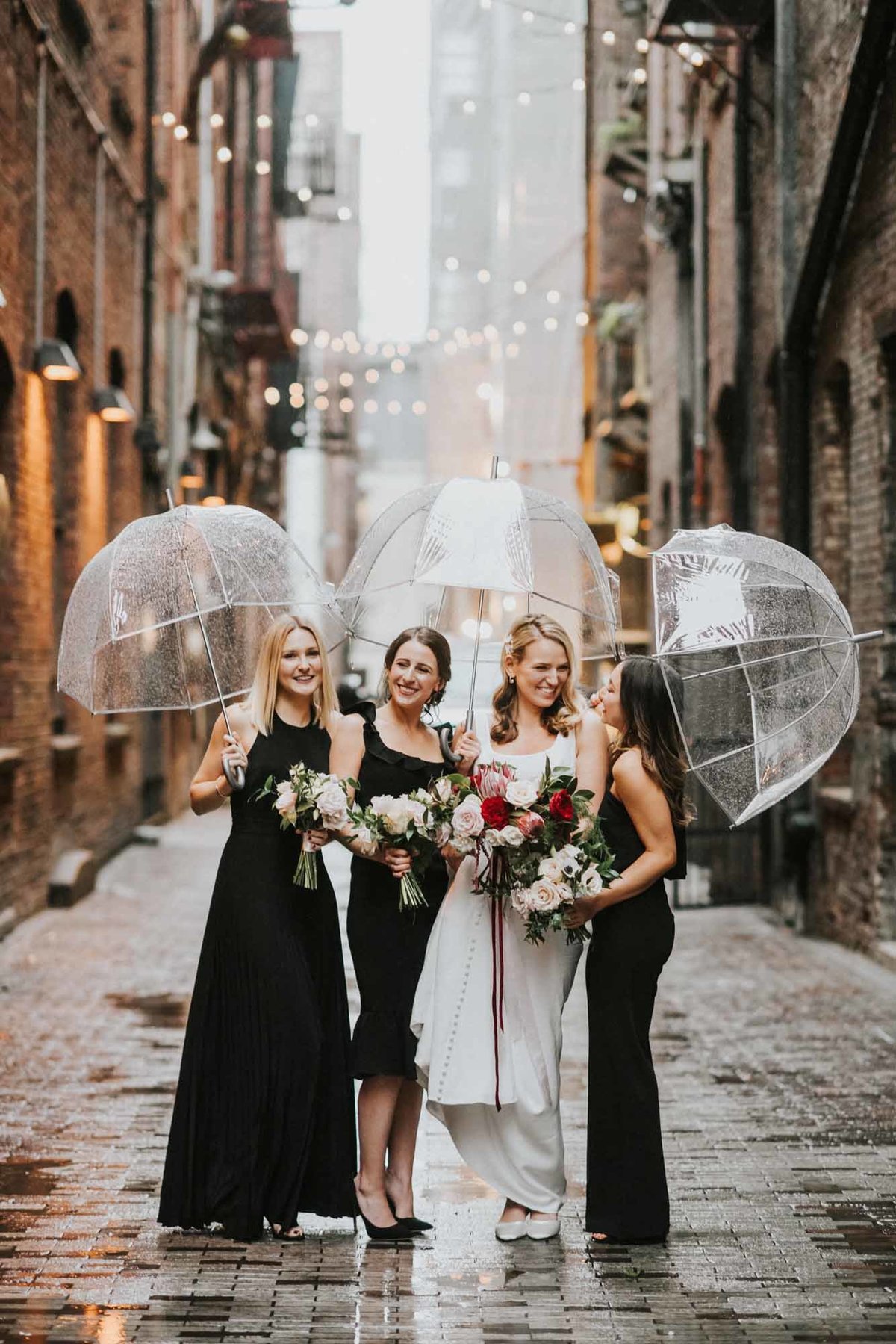 Bride and bride's maids in black dresses, in Seattle alley in the rain, with clear umbrellas