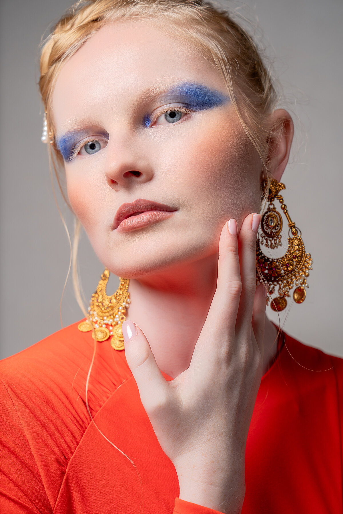 Woman with bright blue eyeliner and red dress holding hand under chin.