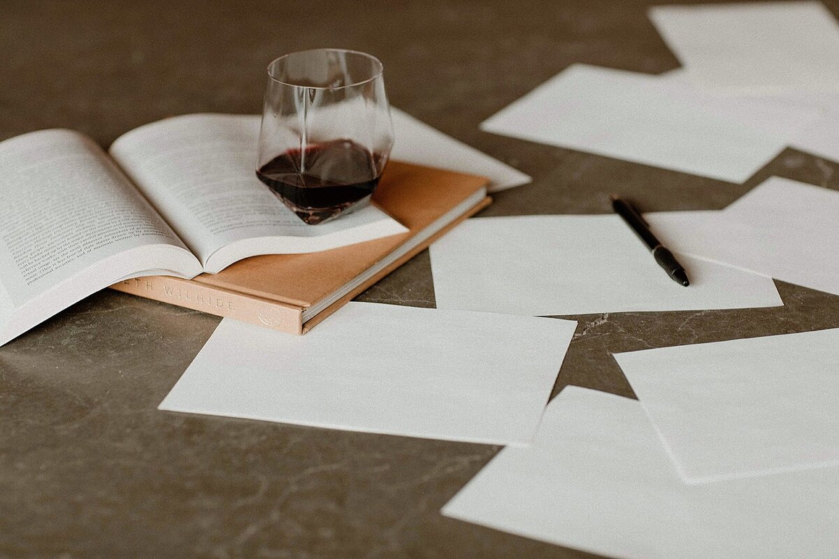 A stack of website copywriting resources for small businesses with a glass of wine on top