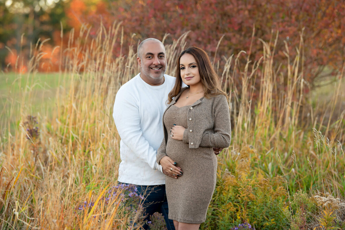 mom and dad to be cradling mom's belly in a Toronto field in the fall .