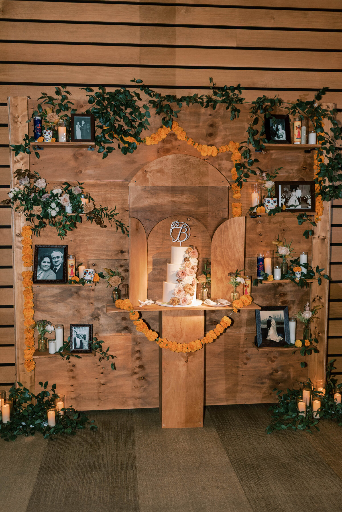 Wooden wedding reception backdrop lit with candles and decorated with greenery and framed photographs