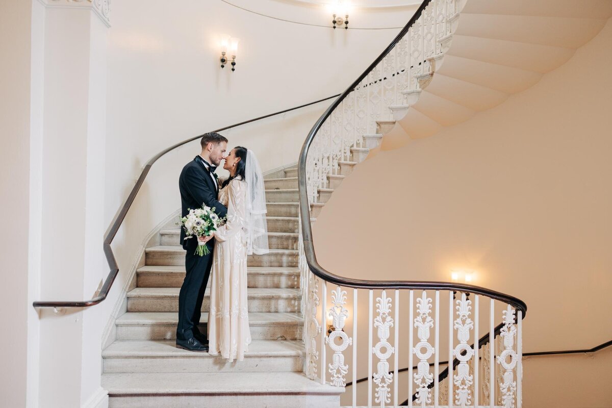 Bride and groom sharing a kiss on an elegant staircase.